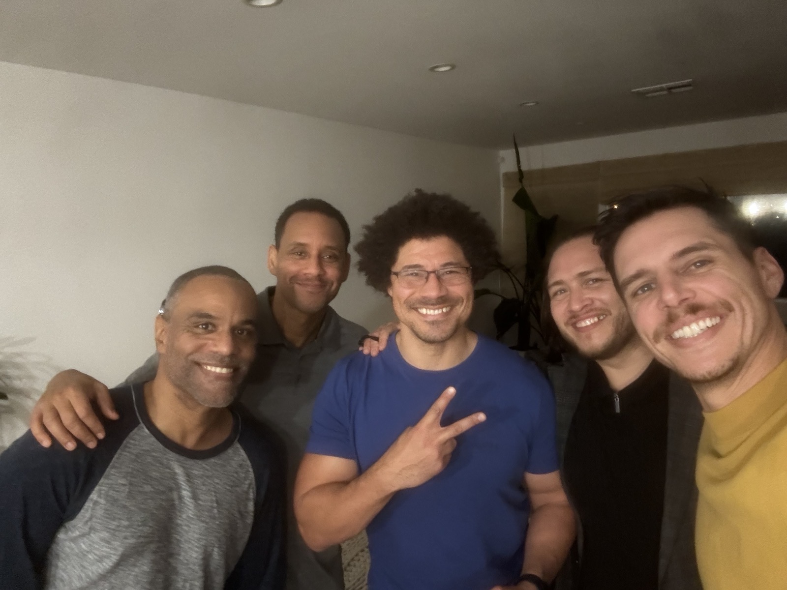 Five men leaning together for a warm group photo in a living room