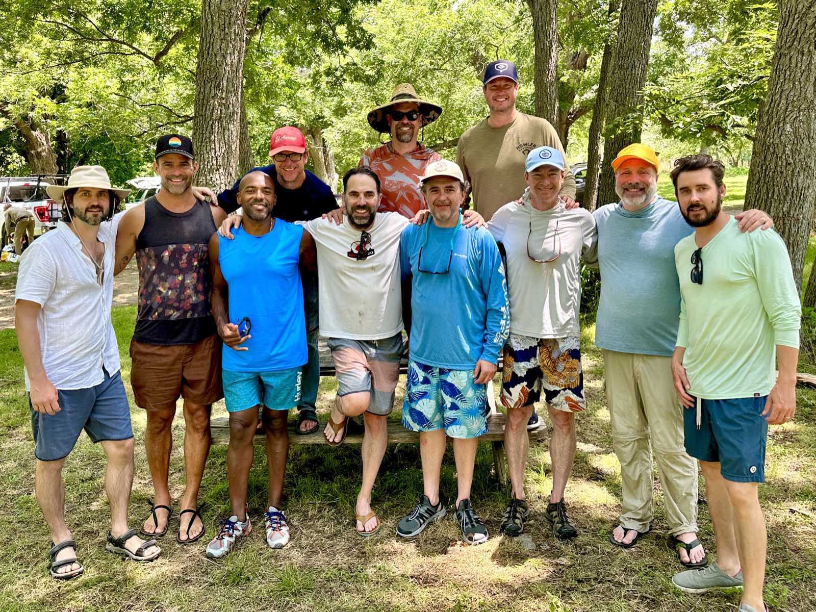 Eleven men posed together in a wooded clearing