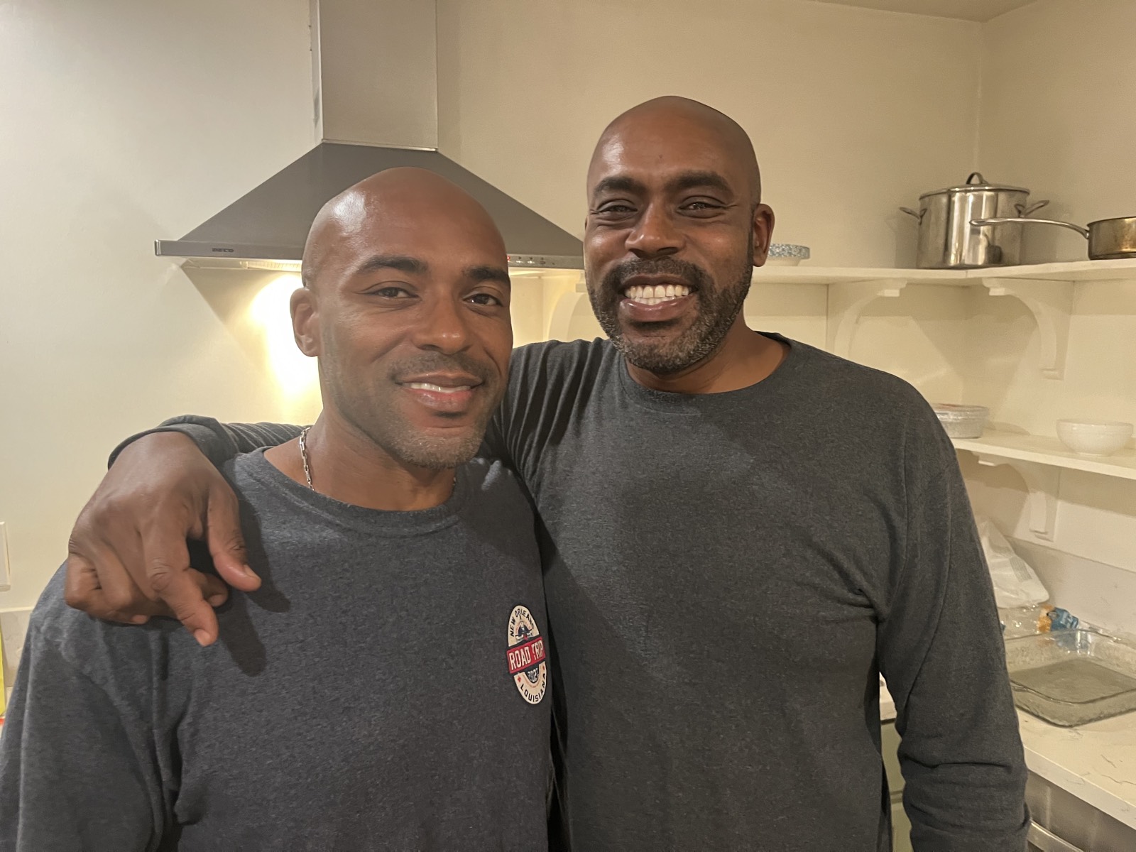 Two men in a kitchen with arms around each other, broad genuine smiles