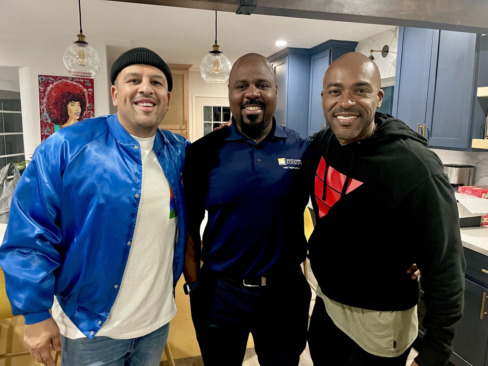 Three men in a modern kitchen with arms around shoulders, all smiling